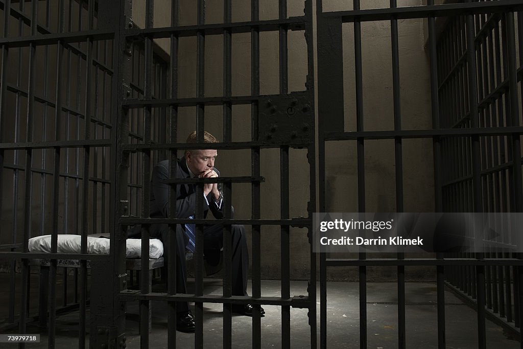 Mature businessman sitting on bed in prison cell