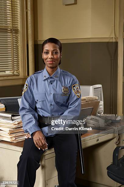 young policewoman sitting on desk, smiling, portrait - police sitting stock-fotos und bilder