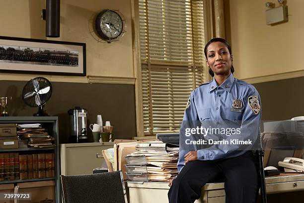 young policewoman sitting on desk, portrait - police station foto e immagini stock