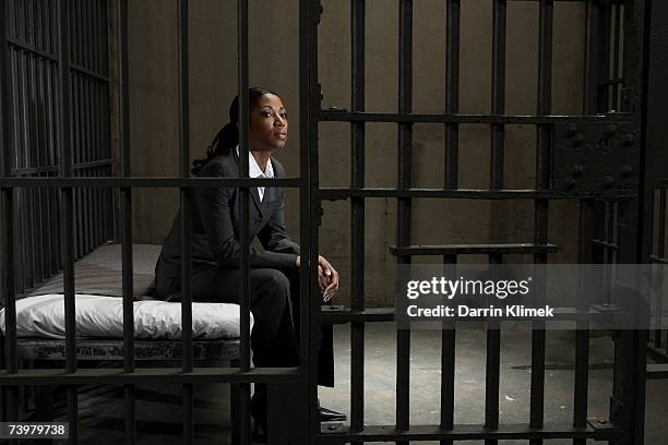 young businesswoman sitting on bed in prison cell, looking away - women in prison stock pictures, royalty-free photos & images