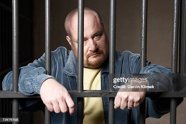 bald mid-adult man standing behind prison bars - bald man foto e immagini stock