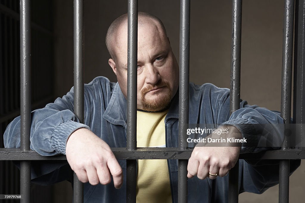 Bald mid-adult man standing behind prison bars