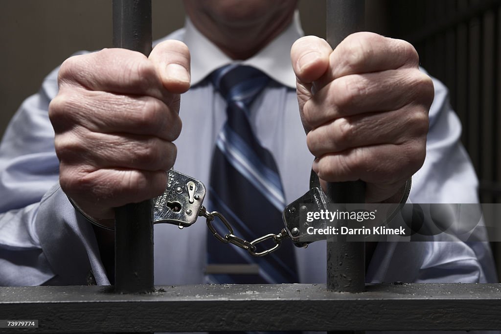 Man in handcuffs, holding prison bars, mid section, close-up of hands