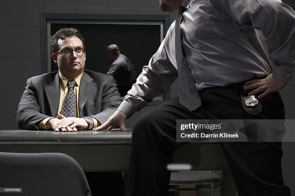 Two men sitting at desk in interrogation room