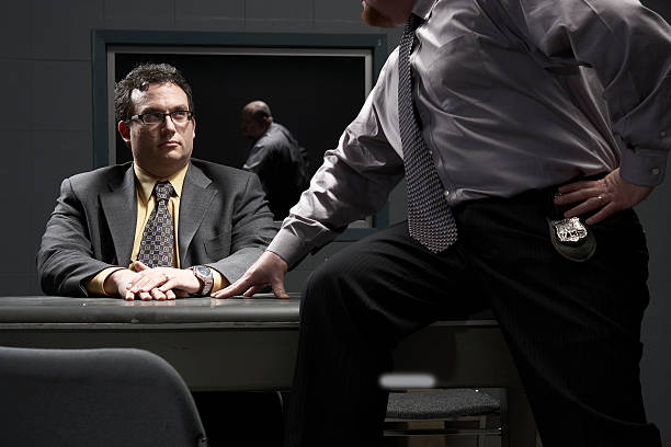 two men sitting at desk in interrogation room - interrogation stock pictures, royalty-free photos & images