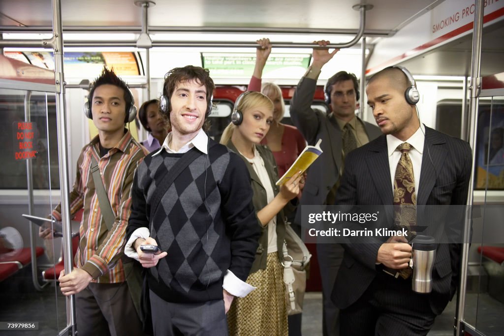 Medium group of people standing in subway train, wearing headphones
