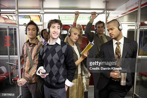 medium group of people standing in subway train, wearing headphones - medium group of people imagens e fotografias de stock