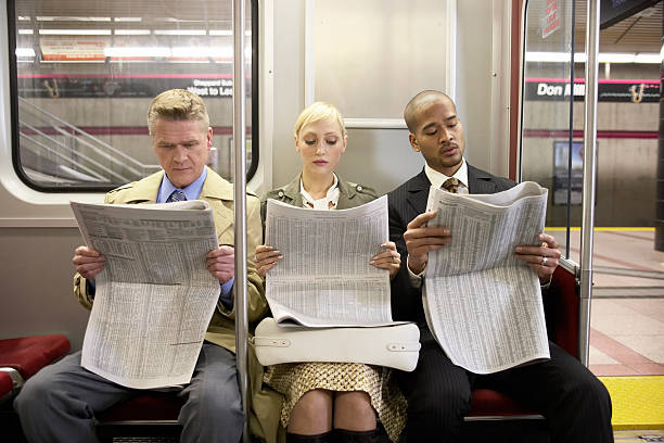 Two men and woman sitting in subway train side by side, reading newspaper