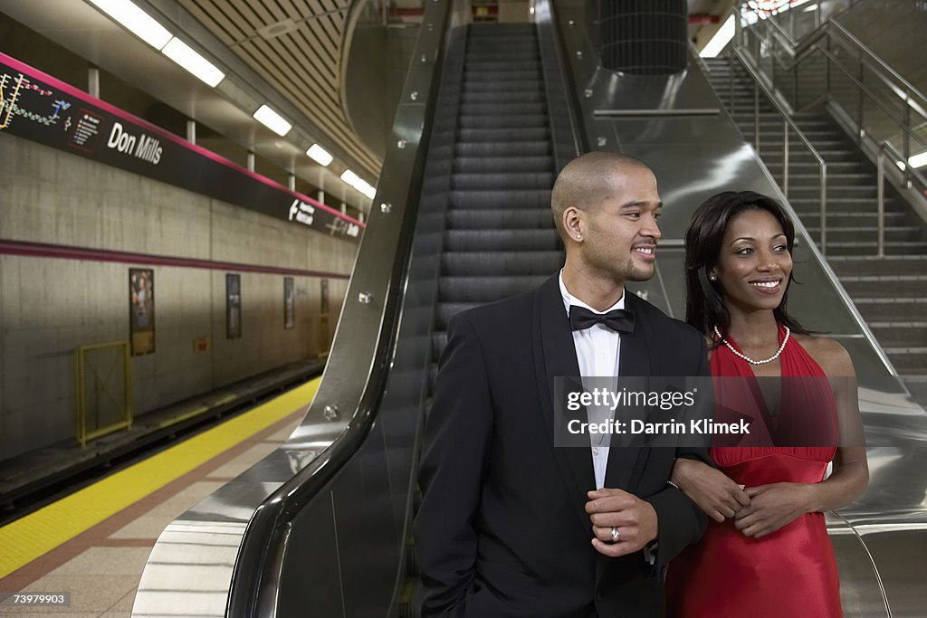 Young man and young woman in subway platform, wearing evening clothes