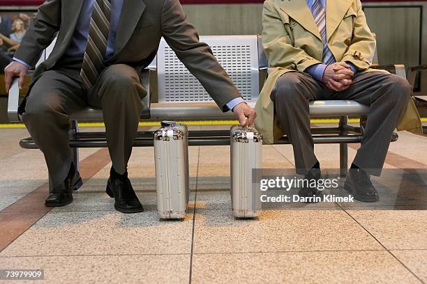 two identical briefcases in front of two men sitting on bench, man on the left touching briefcase on the right - shade45 stock pictures, royalty-free photos & images