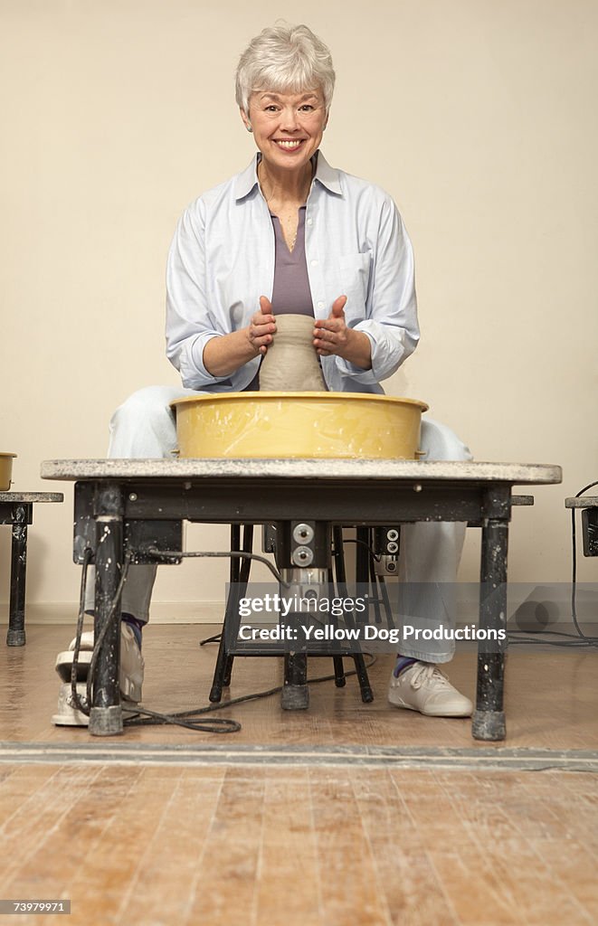 Senior woman moulding clay on wheel in art studio, portrait