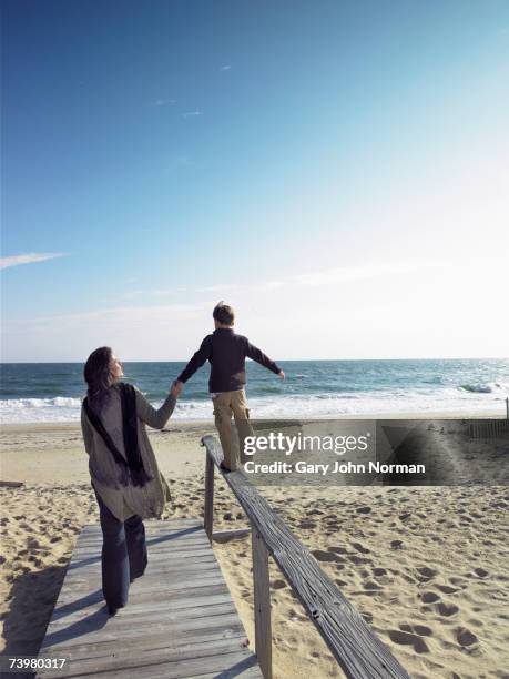 mother holding hand of son (6-8) walking on railing, rear view - gary balance foto e immagini stock