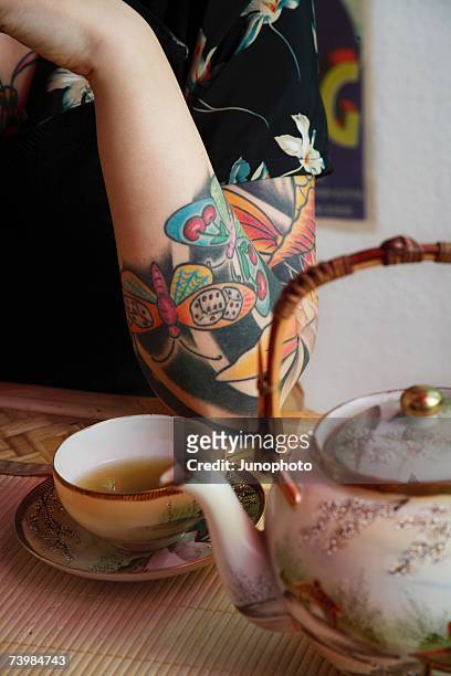 woman's tattooed arm resting next to japanese tea set - butterfly tattoos stock pictures, royalty-free photos & images