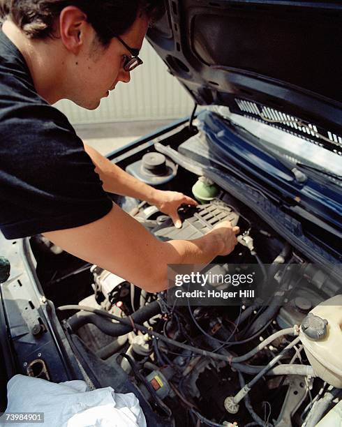 young man checking a car battery - autobatterie stock-fotos und bilder