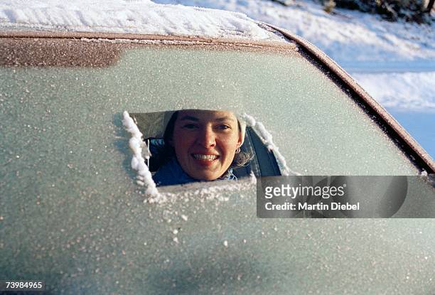 woman sitting in car a and peeking through a frost covered windshield - winter car window stock pictures, royalty-free photos & images