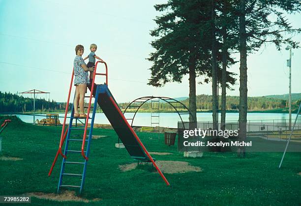 a mother standing at the top of a slide with her young son - mother and son at playground stock-fotos und bilder