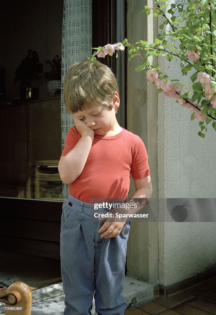 Boy standing in doorway resting his head in his hand