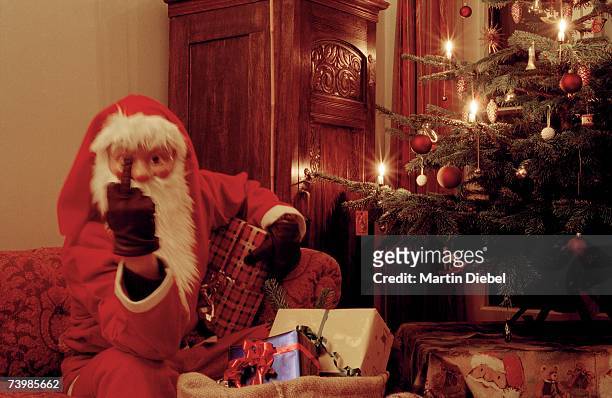 santa claus raising his middle finger whilst sitting on a sofa next to an illuminated christmas tree - middle finger funny 個照片及圖片檔