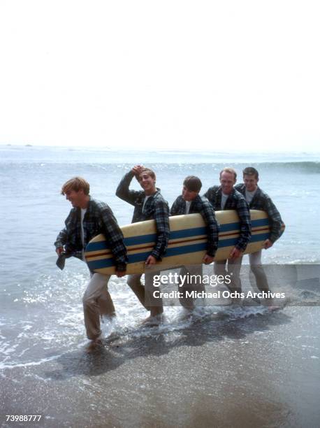 Rock and roll band "The Beach Boys" walk along the beach holding a surfboard for a portrait session in August 1962 in Los Angeles, California. Dennis...