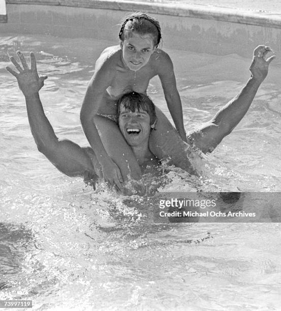 Actor and body builder Arnold Schwarzenegger plays with a topless Nastassja Kinski on his shoulders in a pool in 1976 in Los Angeles, California.