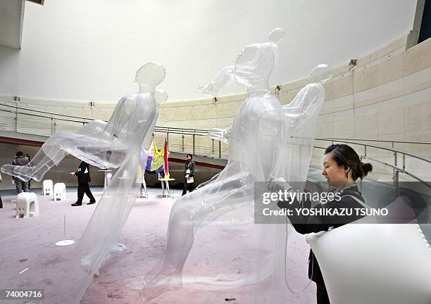 Staff pumps helium gas into human-shaped plastic balloons fitted with ultra-light-weight super-organza fabric clothes installed by contemporary...