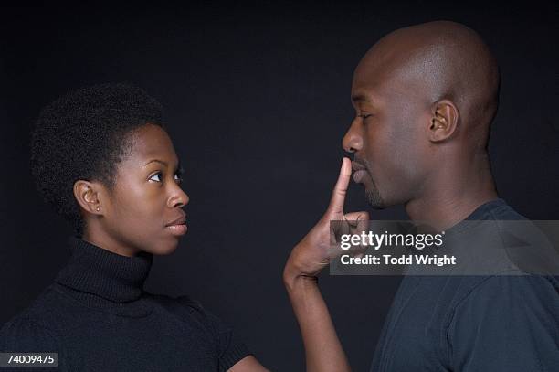 african woman putting finger on boyfriend's lips - finger in mouth stockfoto's en -beelden