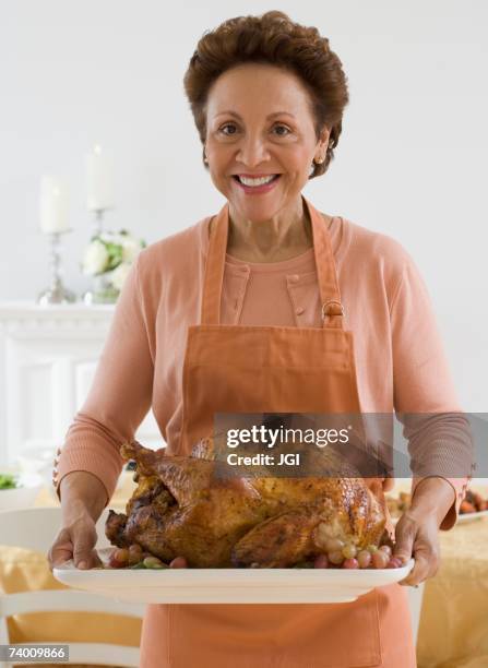 senior hispanic woman holding roast turkey - frau mit tablett stock-fotos und bilder