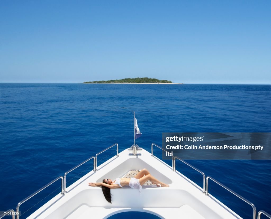 Pacific Islander woman sunbathing on bow of yacht
