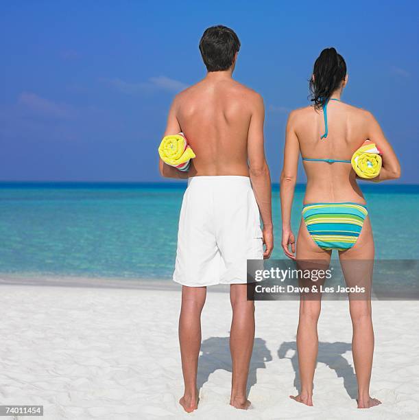 couple holding towels at beach - badehose stock-fotos und bilder