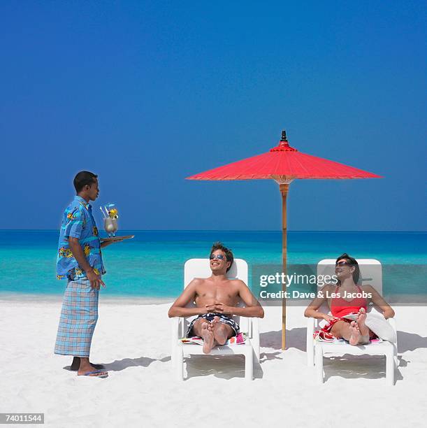 maldivian man serving drinks to couple at beach - pechos de mujer playa fotografías e imágenes de stock