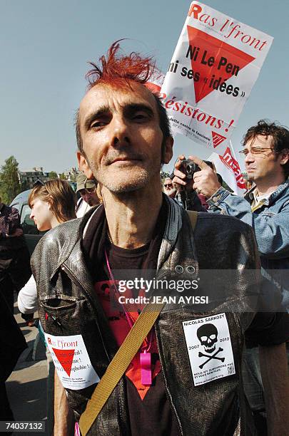 Man presents his stickers as an other holds a poster reading : "Ras l'Front" , neither Le Pen, neither his ideas, let us resist" in the rally...