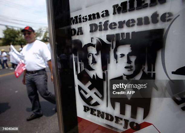 San Salvador, EL SALVADOR: Salvadorean workers walk next to a graffiti tag which compares Adolf Hitler with US President George W.Bush during the May...