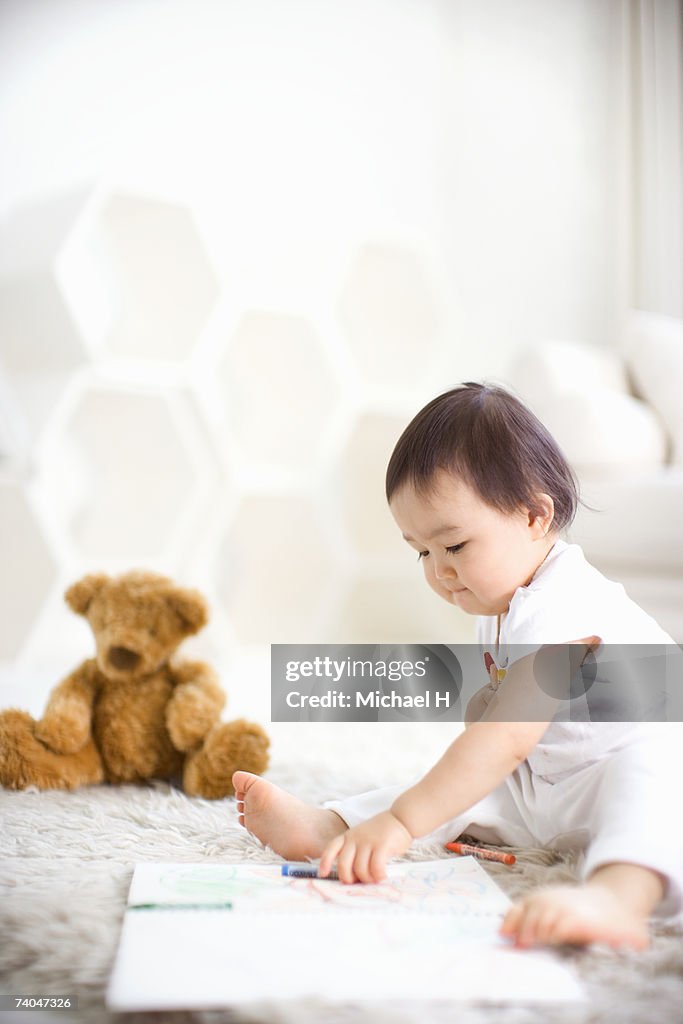 Baby girl (15-18 months) sitting on rug, drawing