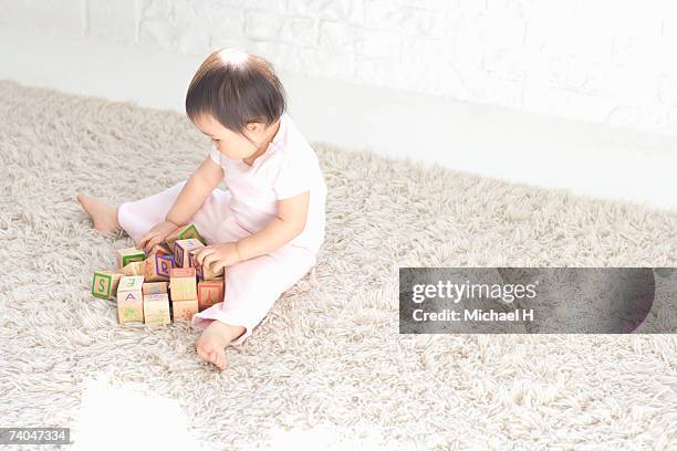 baby girl (15-18 months) sitting on rug, playing with wooden alphabet blocks, elevated view - one baby girl only - fotografias e filmes do acervo