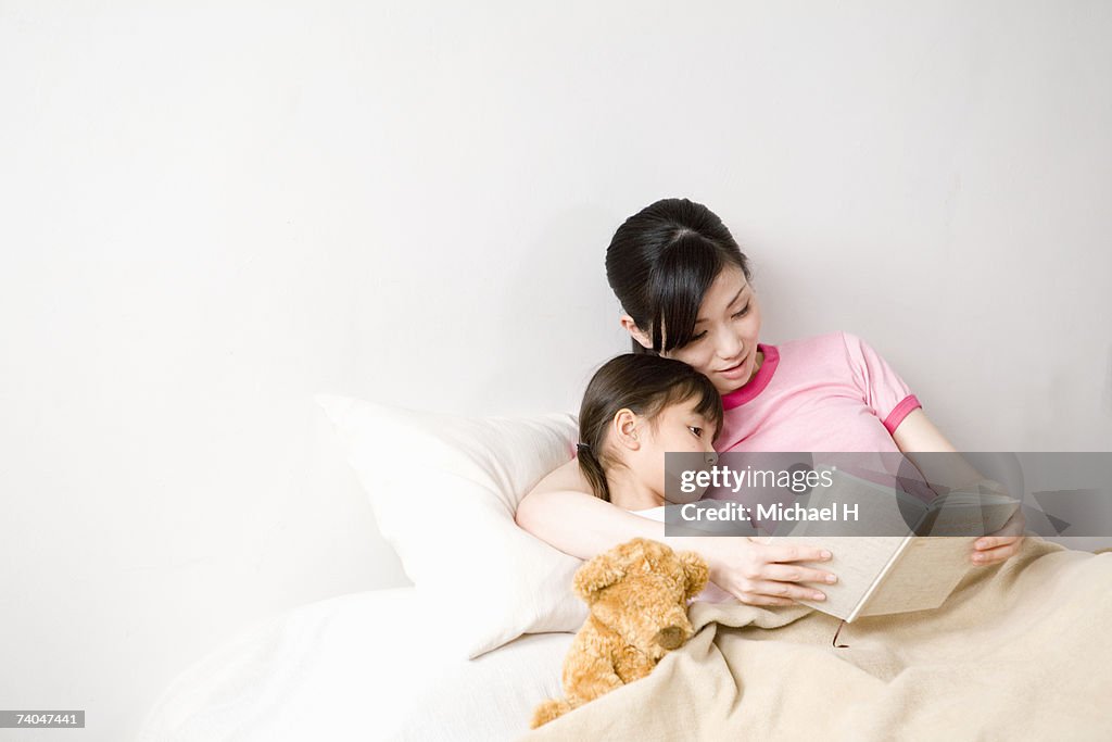 Mother and daughter (6-7) reading book in bed