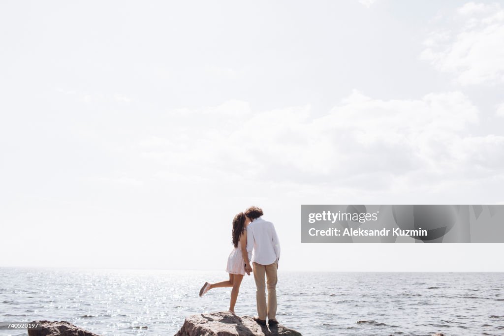 Middle Eastern couple kissing on rocks near ocean