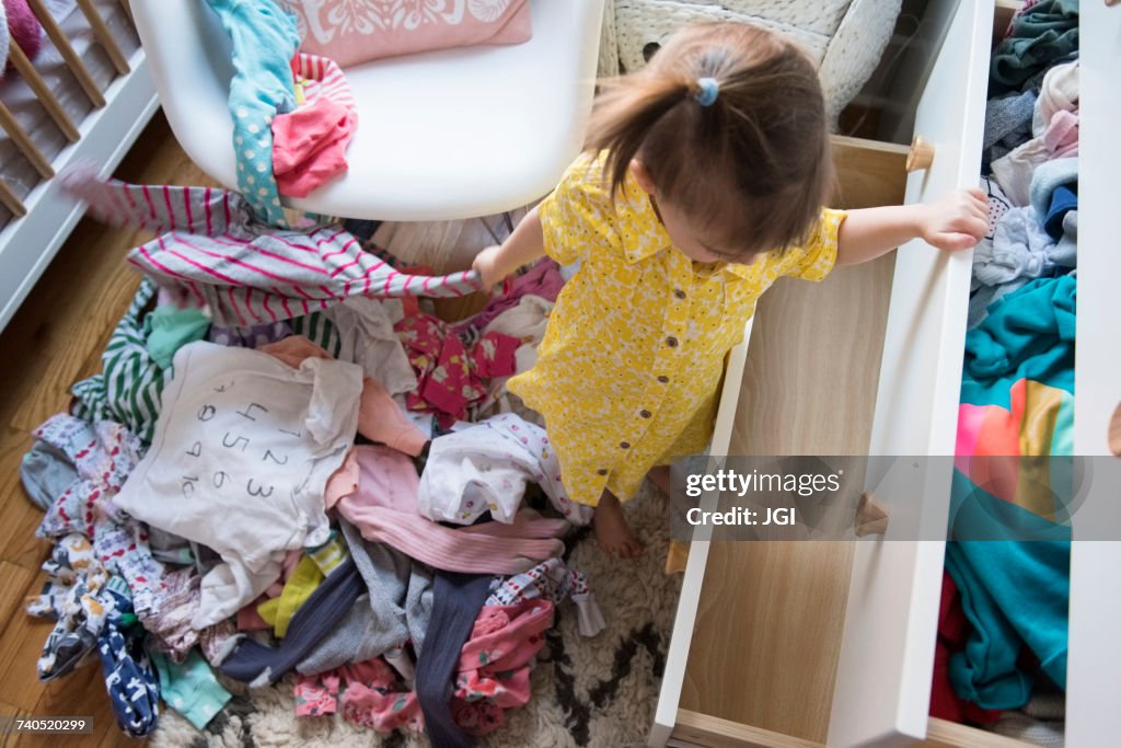 Caucasian baby girl removing clothing from dresser drawer