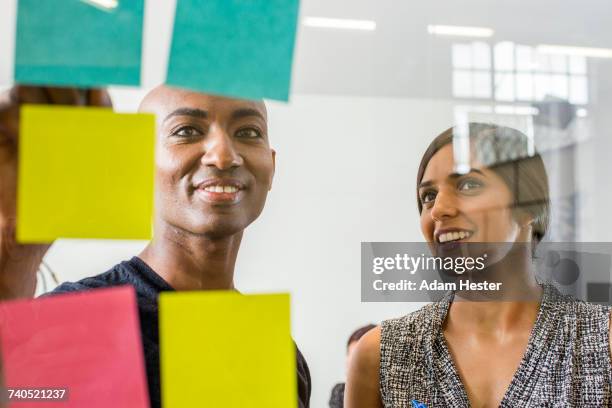 woman and man reading adhesive notes in office - african american and happy and close up and office stock pictures, royalty-free photos & images
