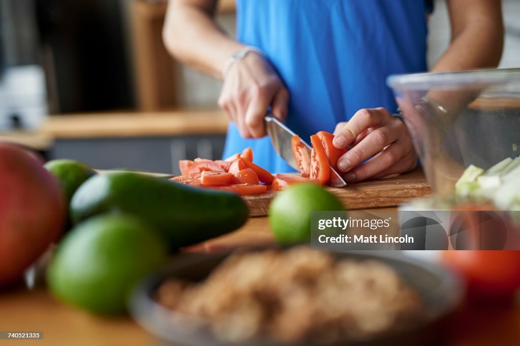 Hands of young woman at kitchen table slicing tomatoes