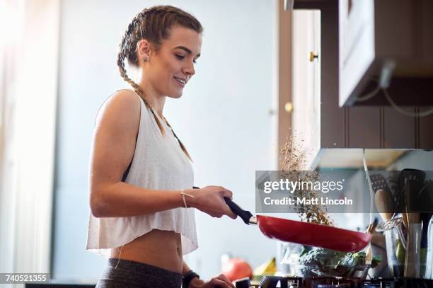 young woman drinking tossing toasted nuts at kitchen hobs - sartenes fotografías e imágenes de stock