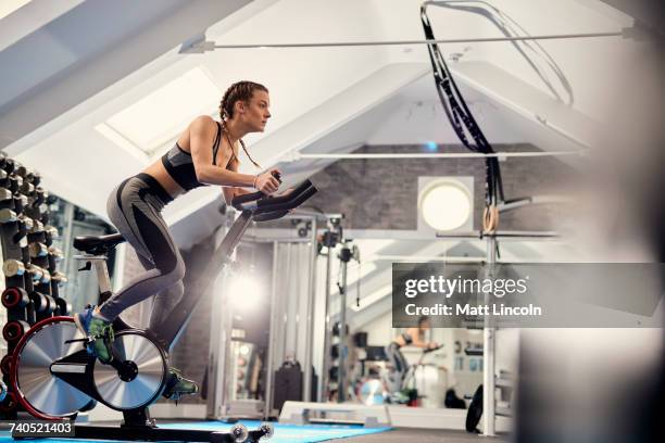 young woman training, pedalling exercise bike in gym - gym interior stock pictures, royalty-free photos & images