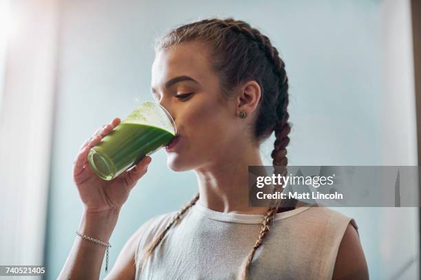 young woman drinking vegetable smoothie in kitchen - smoothie stock-fotos und bilder