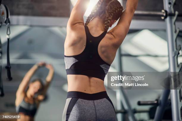 young woman training, looking in mirror while stretching arms in gym - gym training fotografías e imágenes de stock