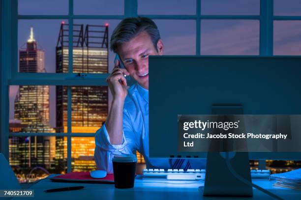 smiling caucasian businessman using computer and talking on cell phone - white night melbourne stock pictures, royalty-free photos & images