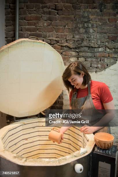 smiling caucasian woman placing cup in pottery kiln - pottery kiln stock pictures, royalty-free photos & images