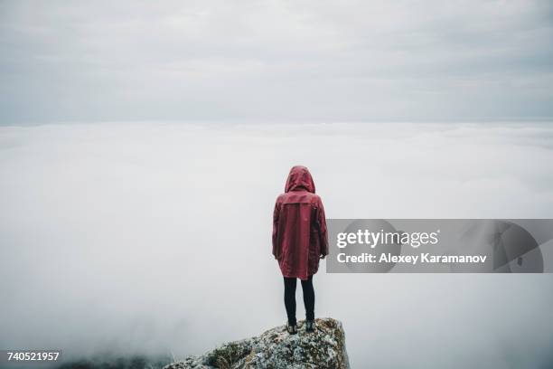 distant caucasian woman standing on rock watching fog on ocean - fog isolated stock pictures, royalty-free photos & images