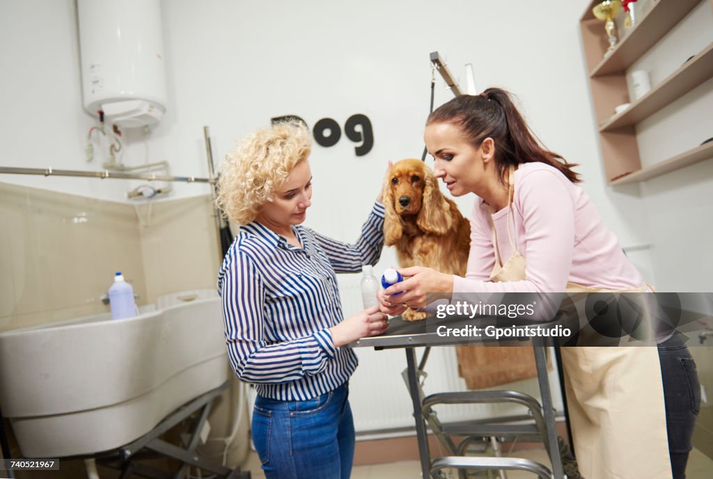 Female groomer selling shampoo to customer at dog grooming salon