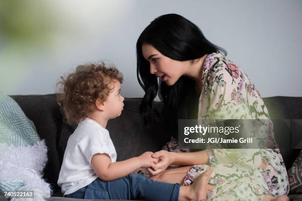 caucasian mother sitting on sofa holding hands and talking with son - ammonite foto e immagini stock