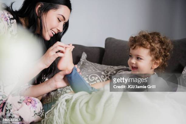 caucasian mother sitting on sofa playing with toes of son - laughing teen stockfoto's en -beelden
