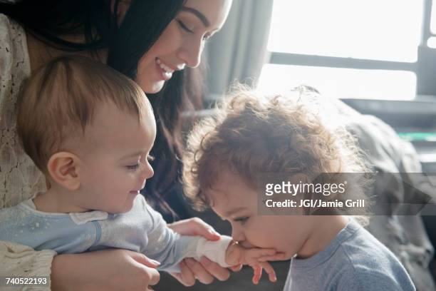 caucasian mother watching son kiss hand of baby brother - middle sibling stock pictures, royalty-free photos & images